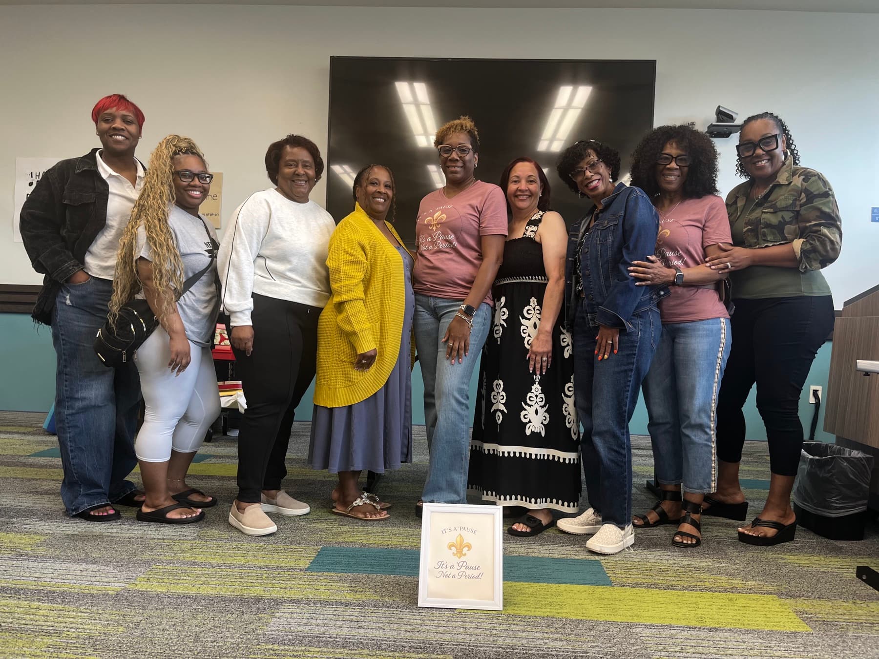 Nine women together at IPNP’s first community meeting with the framed original IPNP sign in front